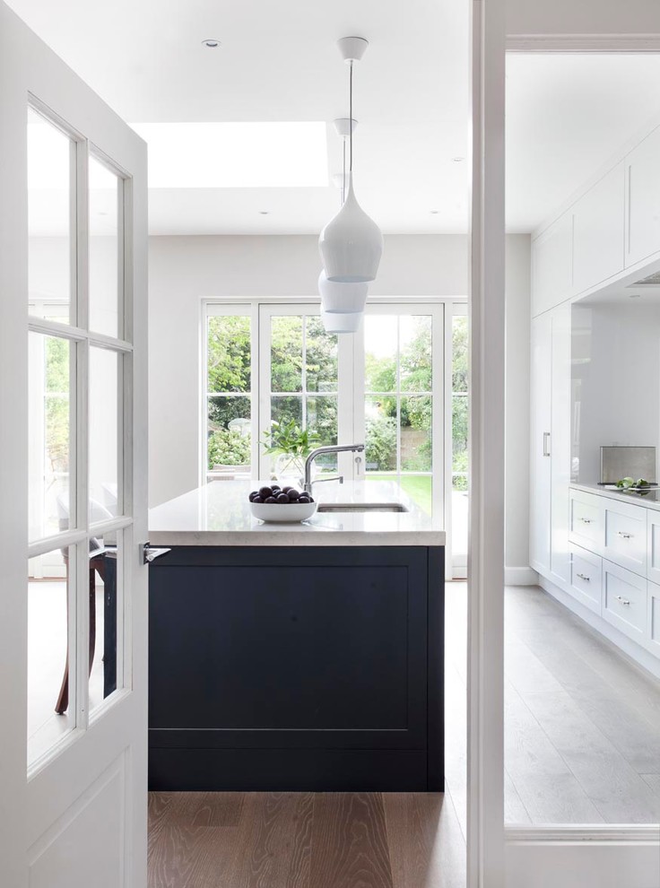 This is an example of a mid-sized modern single-wall eat-in kitchen in Dublin with shaker cabinets, quartzite benchtops, black appliances, medium hardwood floors and with island.