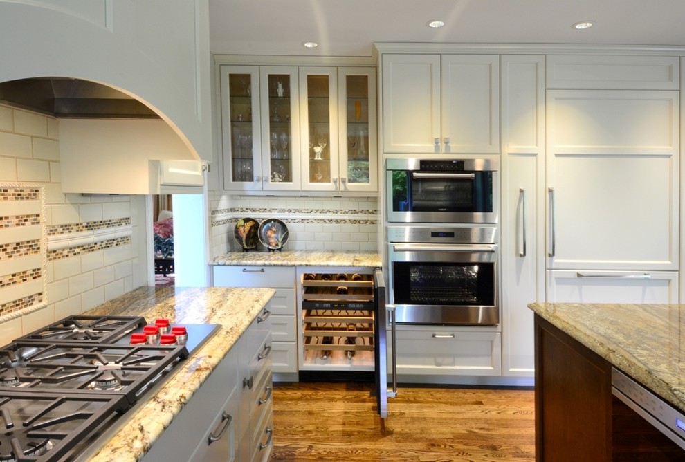Large transitional l-shaped medium tone wood floor open concept kitchen photo in Seattle with a single-bowl sink, recessed-panel cabinets, white cabinets, granite countertops, beige backsplash, ceramic backsplash, stainless steel appliances and an island