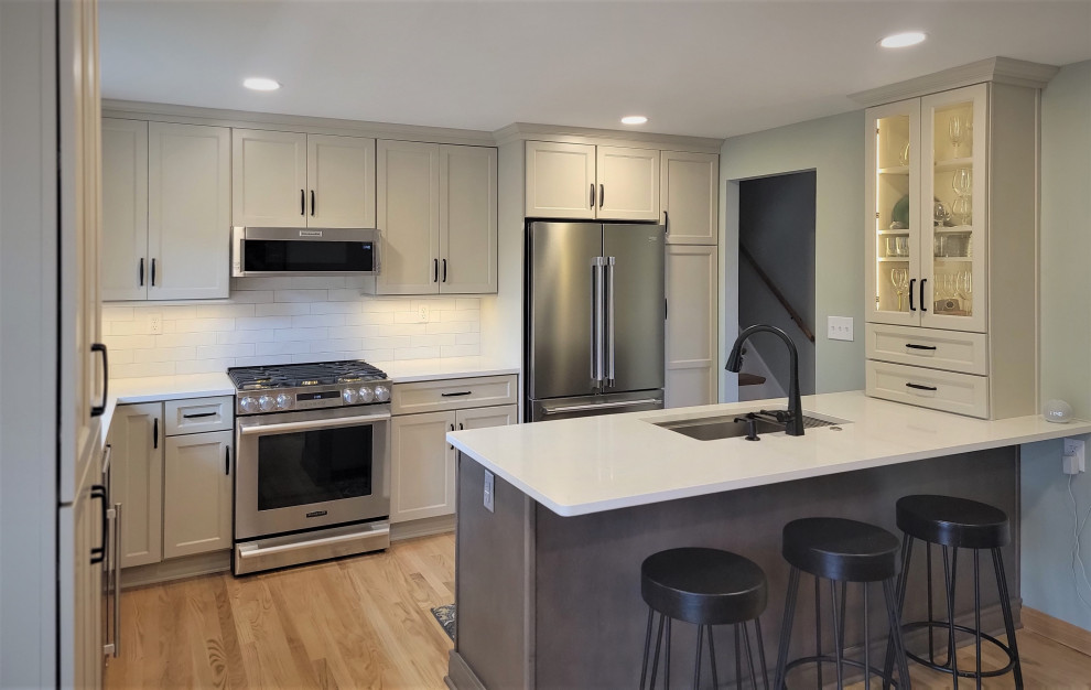 Eat-in kitchen - mid-sized transitional l-shaped medium tone wood floor and yellow floor eat-in kitchen idea with an undermount sink, flat-panel cabinets, gray cabinets, quartz countertops, white backsplash, ceramic backsplash, stainless steel appliances, an island and white countertops