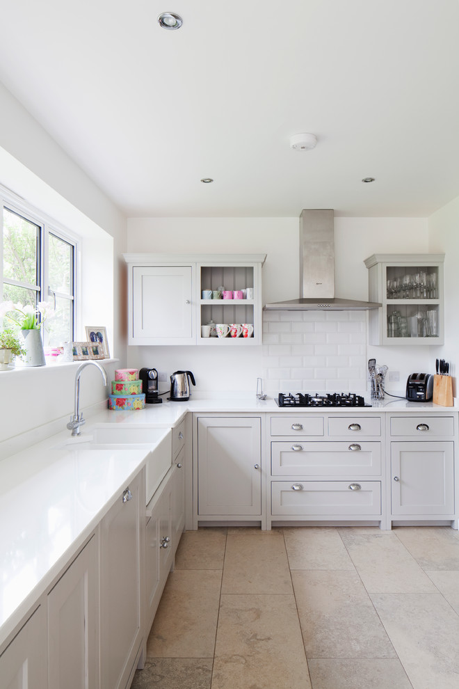 Design ideas for a mid-sized country l-shaped separate kitchen in Surrey with a farmhouse sink, shaker cabinets, grey cabinets, white splashback, subway tile splashback, stainless steel appliances, solid surface benchtops, limestone floors and no island.