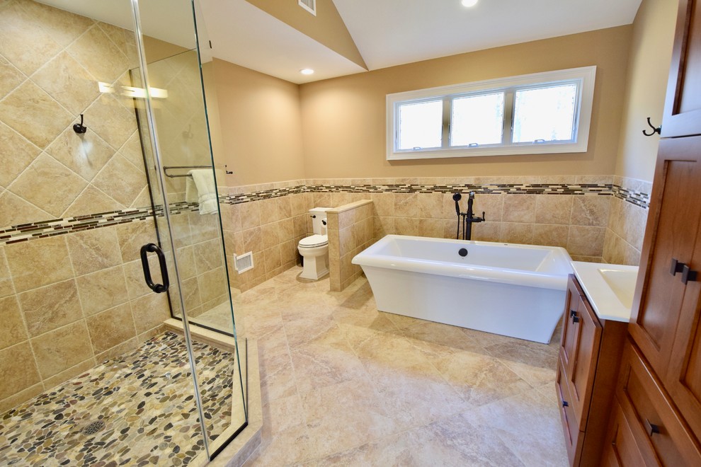 Example of a large transitional master beige tile and ceramic tile ceramic tile and beige floor freestanding bathtub design with recessed-panel cabinets, medium tone wood cabinets, a two-piece toilet, beige walls, a console sink, quartz countertops, a hinged shower door and white countertops
