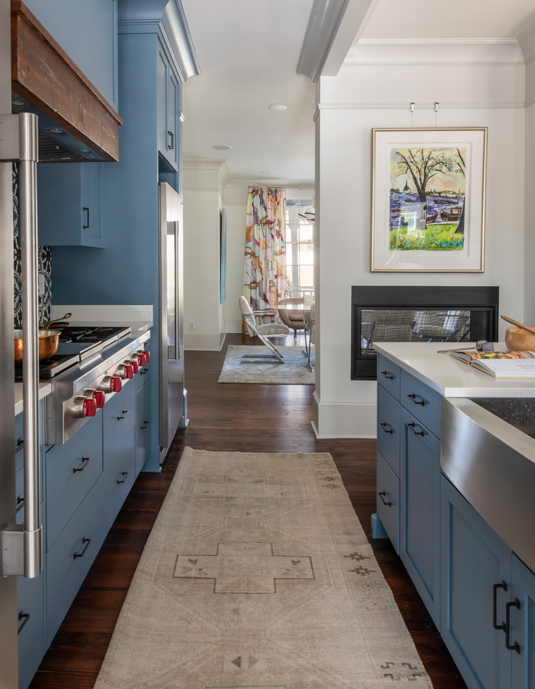 Photo of a mid-sized traditional galley eat-in kitchen in Atlanta with an integrated sink, flat-panel cabinets, blue cabinets, solid surface benchtops, multi-coloured splashback, ceramic splashback, stainless steel appliances, medium hardwood floors, with island, brown floor and white benchtop.