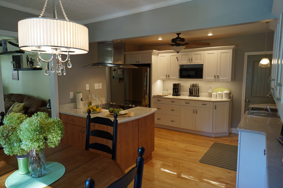 Inspiration for a large transitional l-shaped light wood floor eat-in kitchen remodel in Boston with a farmhouse sink, shaker cabinets, white cabinets, quartz countertops, white backsplash, stone slab backsplash, stainless steel appliances and an island
