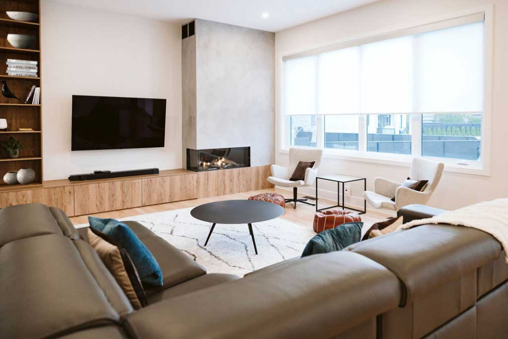 This is an example of a large modern open plan living room in Montreal with beige walls, light hardwood flooring, a corner fireplace, a concrete fireplace surround and a wall mounted tv.