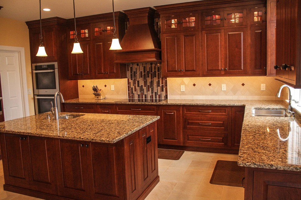 This is an example of a large traditional u-shaped kitchen in Philadelphia with a double-bowl sink, raised-panel cabinets, dark wood cabinets, beige splashback, porcelain splashback, stainless steel appliances, porcelain floors, with island and granite benchtops.