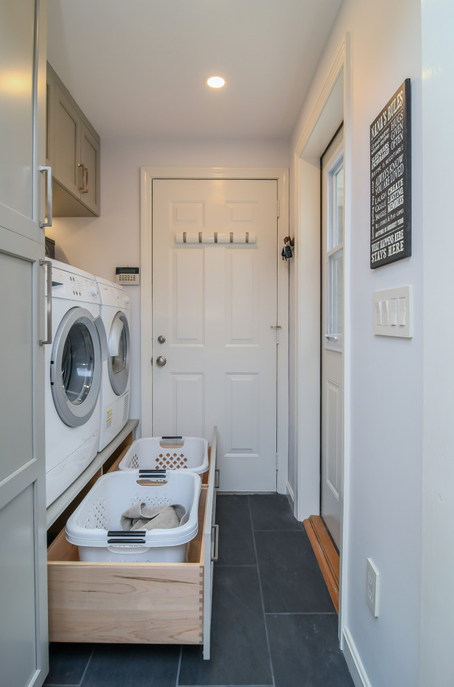 Klassisk inredning av en linjär tvättstuga, med grå skåp, grå väggar, klinkergolv i porslin, en tvättmaskin och torktumlare bredvid varandra och svart golv