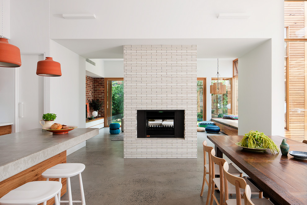 Mid-sized contemporary kitchen/dining combo in Melbourne with white walls, concrete floors, a two-sided fireplace and a tile fireplace surround.