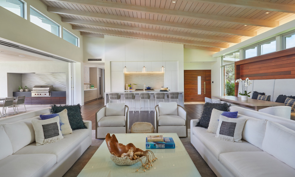 This is an example of a mid-sized tropical open concept family room in Hawaii with medium hardwood floors, brown floor, exposed beam and wood walls.
