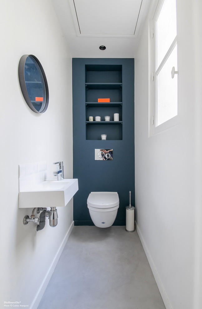 Photo of a mid-sized contemporary powder room in Paris with open cabinets, a wall-mount toilet, blue walls, a wall-mount sink, grey floor, white tile, ceramic tile and concrete floors.