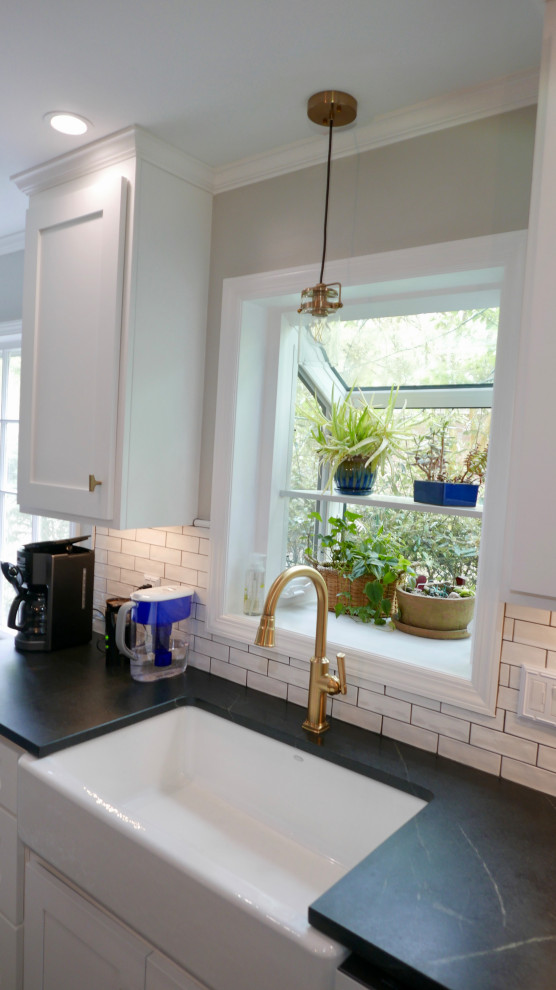 Inspiration for a mid-sized transitional galley porcelain tile and black floor eat-in kitchen remodel with a farmhouse sink, shaker cabinets, white cabinets, soapstone countertops, white backsplash, subway tile backsplash, white appliances, an island and black countertops