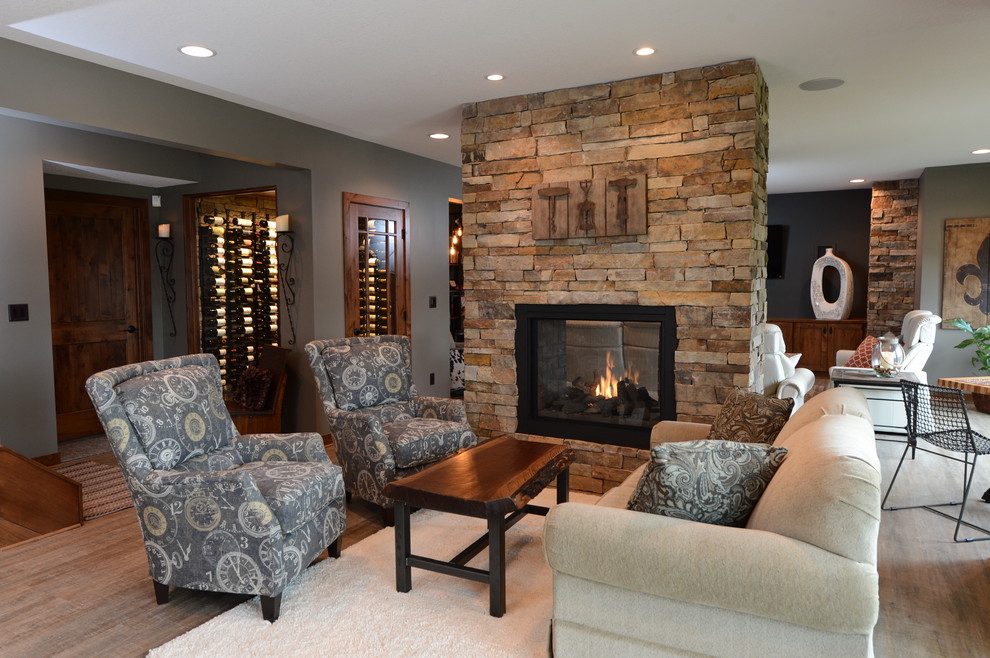 This is an example of a large transitional walk-out basement in Minneapolis with grey walls, light hardwood floors, a two-sided fireplace and a stone fireplace surround.