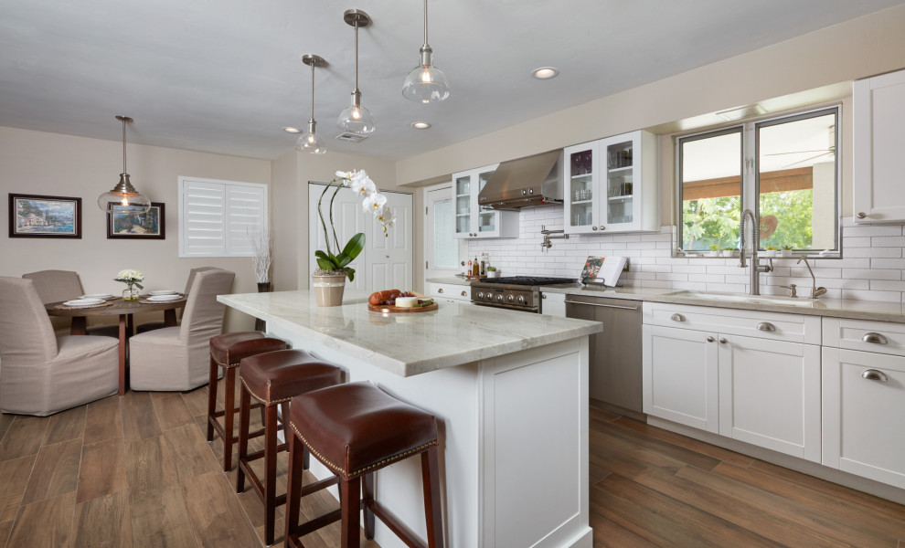 Eat-in kitchen - mid-sized transitional single-wall ceramic tile and brown floor eat-in kitchen idea in Phoenix with an undermount sink, shaker cabinets, white cabinets, granite countertops, white backsplash, subway tile backsplash, stainless steel appliances, an island and gray countertops