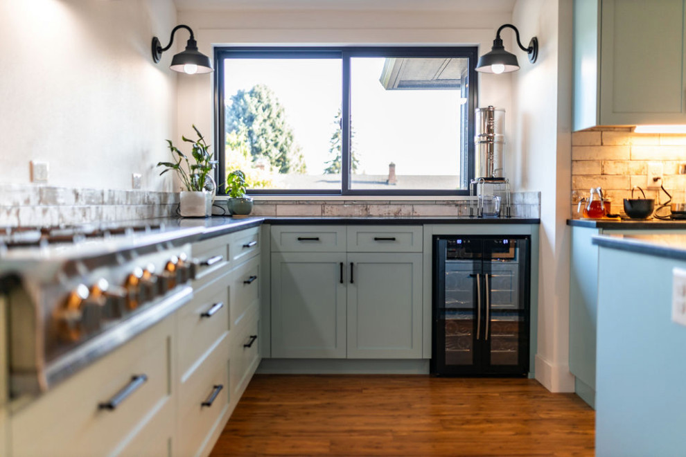 Inspiration for an eclectic kitchen in Portland with shaker cabinets, blue cabinets, soapstone benchtops, ceramic splashback, stainless steel appliances, medium hardwood floors, with island, black benchtop and vaulted.
