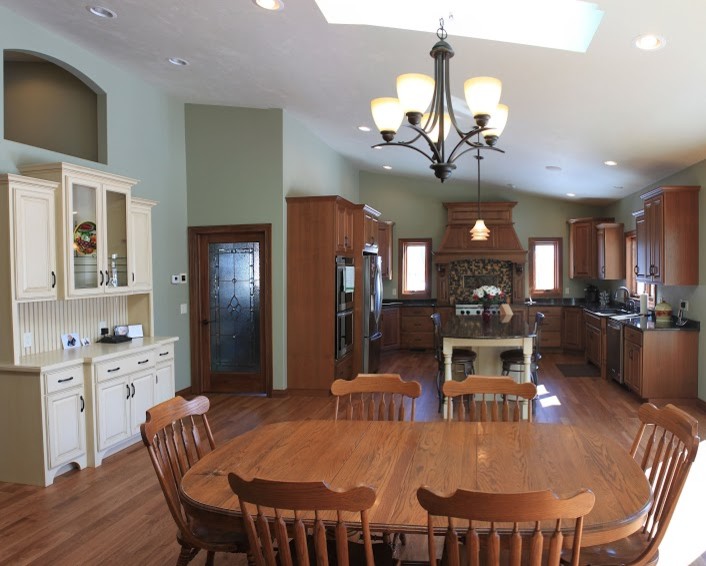 Example of a large galley medium tone wood floor eat-in kitchen design with an undermount sink, raised-panel cabinets, medium tone wood cabinets, quartz countertops, brown backsplash, glass tile backsplash, stainless steel appliances and an island