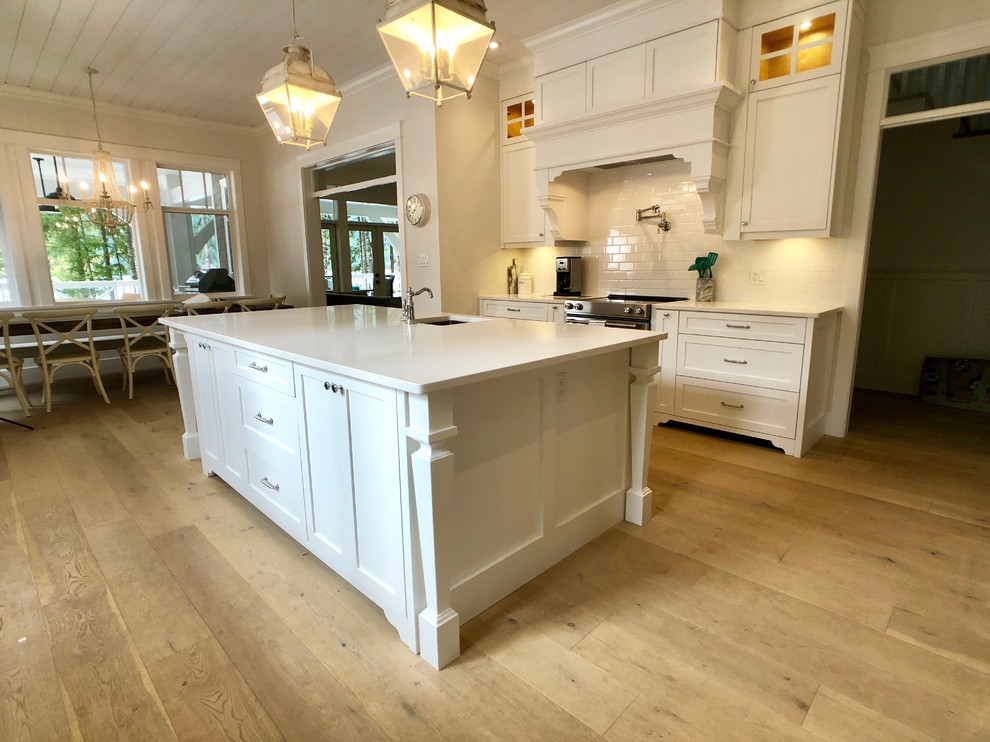 Photo of a large country u-shaped separate kitchen in Other with an undermount sink, shaker cabinets, white cabinets, quartz benchtops, white splashback, subway tile splashback, stainless steel appliances, medium hardwood floors, with island, brown floor and white benchtop.