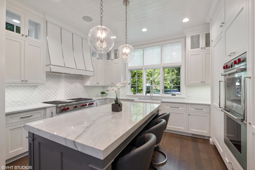 This is an example of a transitional u-shaped separate kitchen in Chicago with a farmhouse sink, white cabinets, quartzite benchtops, white splashback, ceramic splashback, panelled appliances, medium hardwood floors, with island, brown floor and grey benchtop.
