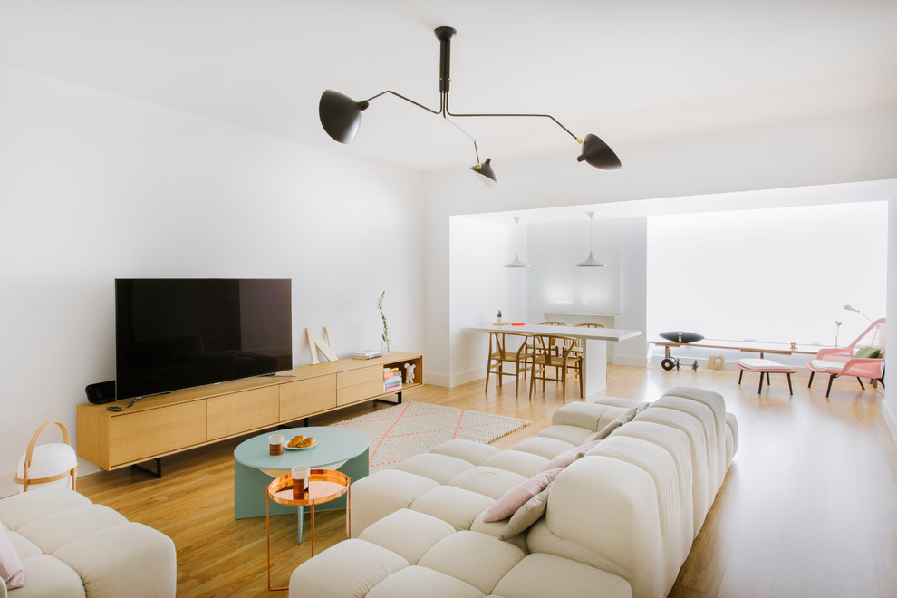 This is an example of a large contemporary formal open concept living room in Madrid with white walls, medium hardwood floors, no fireplace and a freestanding tv.