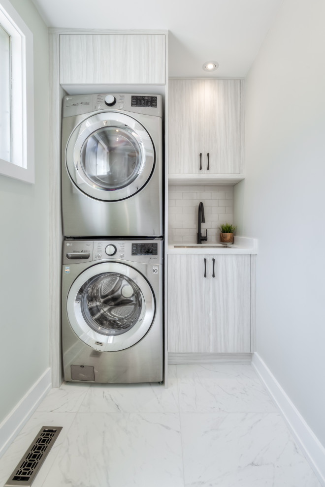 Inspiration for a small contemporary single-wall dedicated laundry room in Toronto with an undermount sink, flat-panel cabinets, grey cabinets, quartz benchtops, beige splashback, ceramic splashback, white walls, porcelain floors, a stacked washer and dryer, white floor and white benchtop.