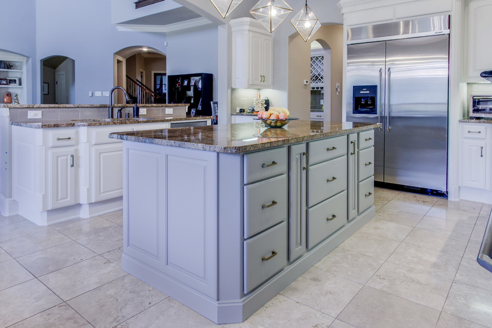 This is an example of a large transitional eat-in kitchen in Dallas with an undermount sink, raised-panel cabinets, grey cabinets, granite benchtops, beige splashback, subway tile splashback, stainless steel appliances, travertine floors, multiple islands, beige floor and brown benchtop.