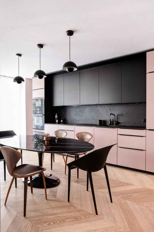 Mid-sized modern single-wall open plan kitchen in Paris with black benchtop, an undermount sink, flat-panel cabinets, pink cabinets, black splashback, black appliances, light hardwood floors, no island and brown floor.