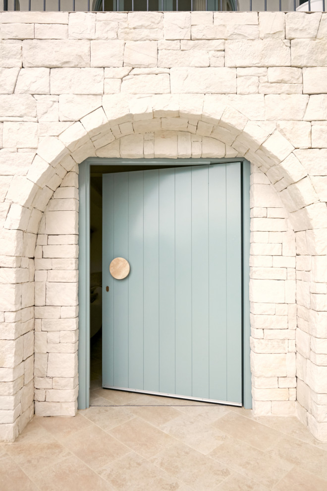 Cette image montre une porte d'entrée méditerranéenne avec un mur beige, un sol en carrelage de porcelaine, une porte pivot, une porte bleue, un sol beige et un mur en parement de brique.