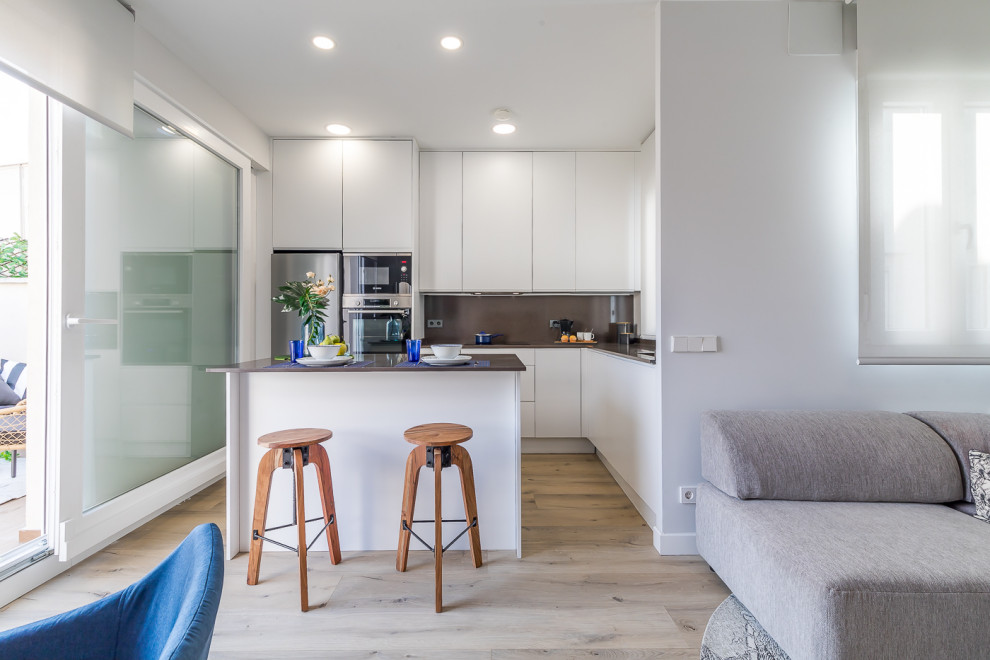This is an example of a small transitional l-shaped eat-in kitchen in Madrid with a single-bowl sink, flat-panel cabinets, white cabinets, limestone benchtops, grey splashback, limestone splashback, stainless steel appliances, medium hardwood floors, with island, brown floor and grey benchtop.