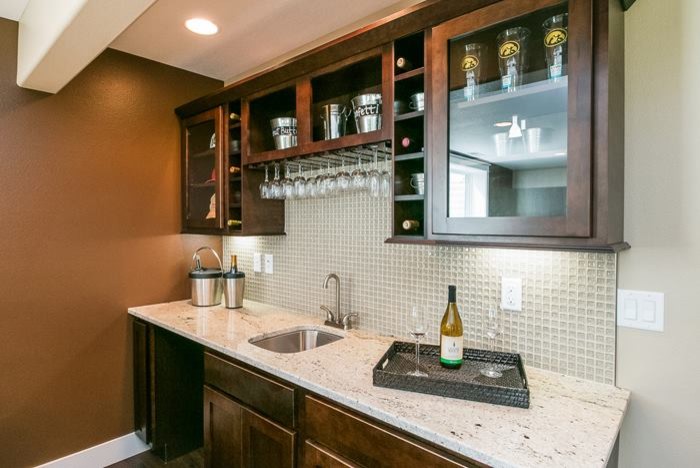 Example of a mid-sized transitional single-wall wet bar design in Cedar Rapids with an undermount sink, glass-front cabinets, dark wood cabinets, quartzite countertops, gray backsplash and glass tile backsplash