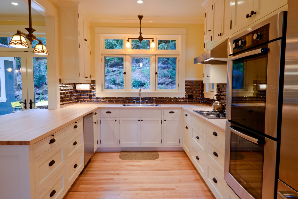 Design ideas for a traditional u-shaped kitchen in Portland with wood benchtops, a drop-in sink, shaker cabinets, white cabinets, black splashback, subway tile splashback and stainless steel appliances.