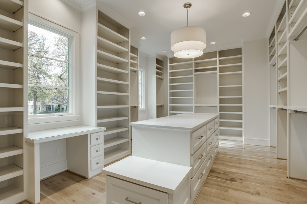 Photo of a mid-sized transitional gender-neutral walk-in wardrobe in Dallas with recessed-panel cabinets, white cabinets and light hardwood floors.