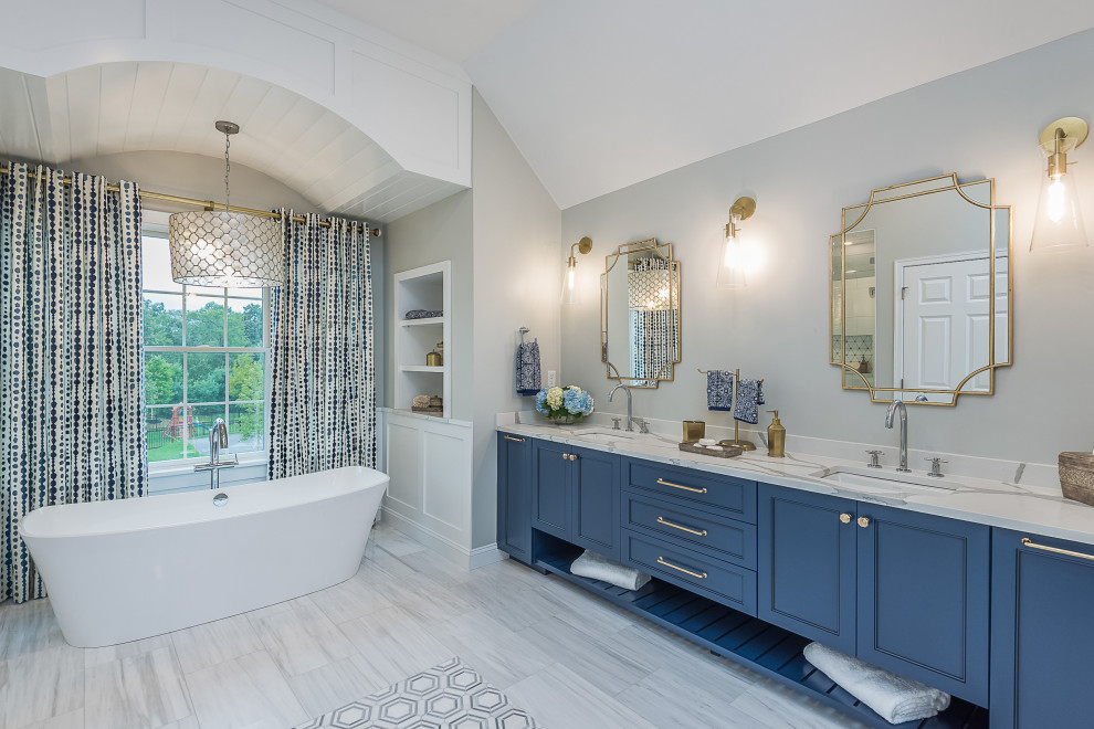 Photo of a large modern master bathroom in Boston with recessed-panel cabinets, blue cabinets, a freestanding tub, a curbless shower, a one-piece toilet, gray tile, ceramic tile, grey walls, ceramic floors, an undermount sink, engineered quartz benchtops, grey floor, a hinged shower door, white benchtops, a shower seat, a double vanity and a built-in vanity.