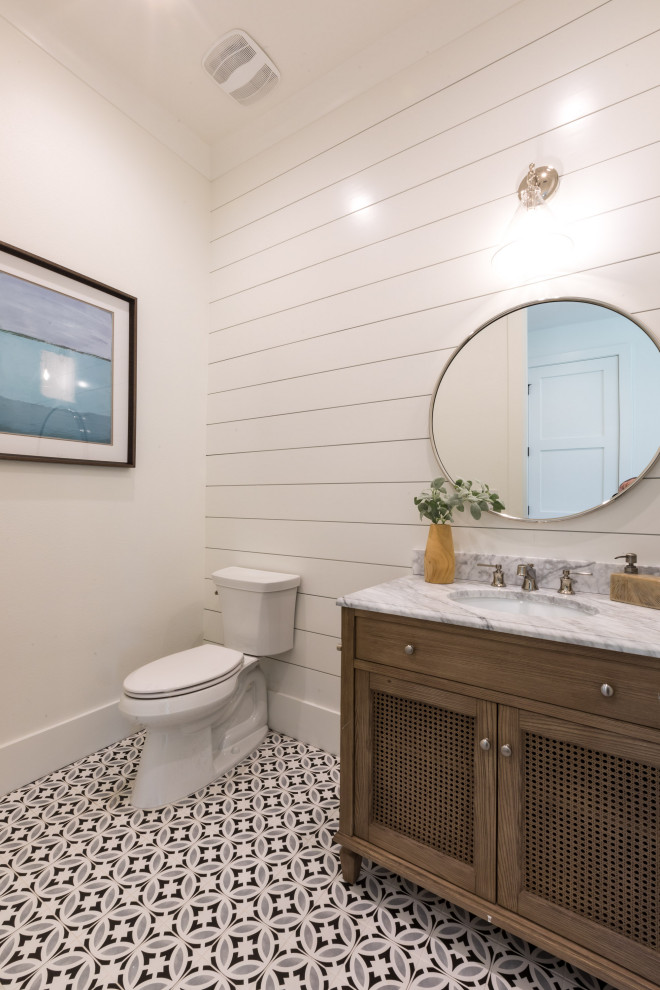 Inspiration for a mid-sized beach style powder room in Orlando with louvered cabinets, brown cabinets, a two-piece toilet, white tile, white walls, porcelain floors, an undermount sink, marble benchtops, blue floor, grey benchtops, a freestanding vanity and planked wall panelling.