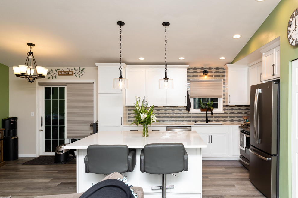 Inspiration for a mid-sized transitional l-shaped open plan kitchen in Seattle with a double-bowl sink, shaker cabinets, white cabinets, quartz benchtops, multi-coloured splashback, porcelain splashback, with island and white benchtop.