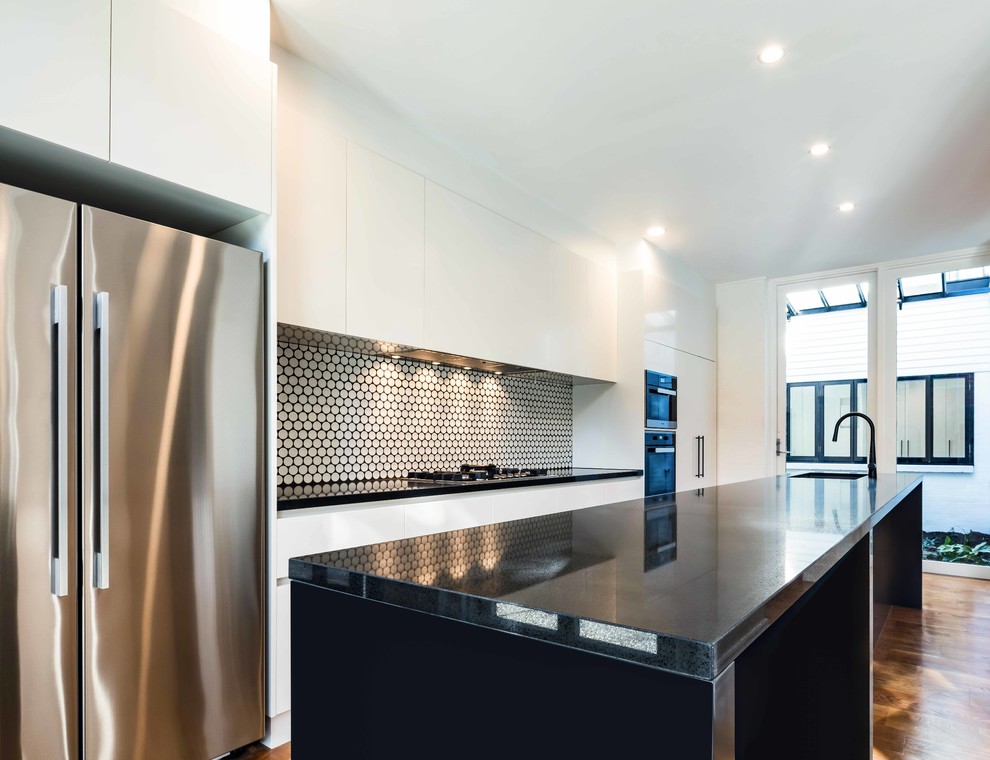 Photo of a contemporary open plan kitchen in Melbourne with a drop-in sink, quartz benchtops, mosaic tile splashback, stainless steel appliances, light hardwood floors, with island and brown floor.