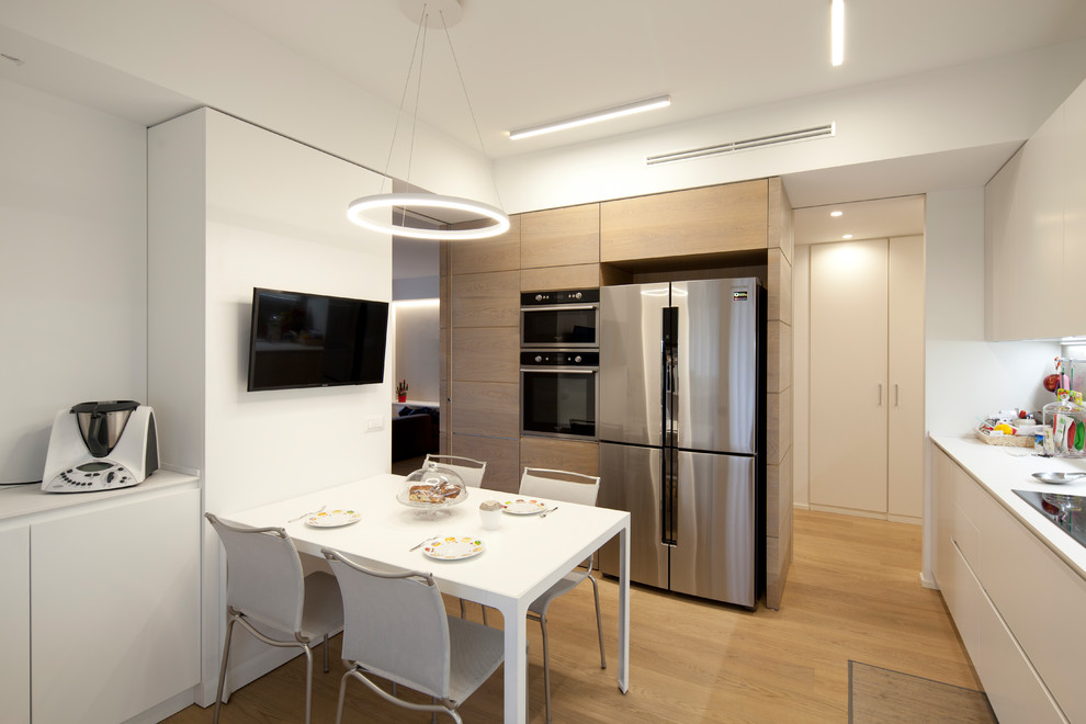 Photo of a mid-sized contemporary single-wall separate kitchen in Milan with an integrated sink, beaded inset cabinets, light wood cabinets, laminate benchtops, grey splashback, timber splashback, stainless steel appliances, light hardwood floors, no island, beige floor and white benchtop.