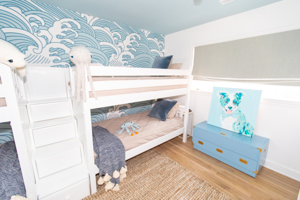 This is an example of a large coastal gender neutral children’s room in Other with blue walls, light hardwood flooring and wallpapered walls.