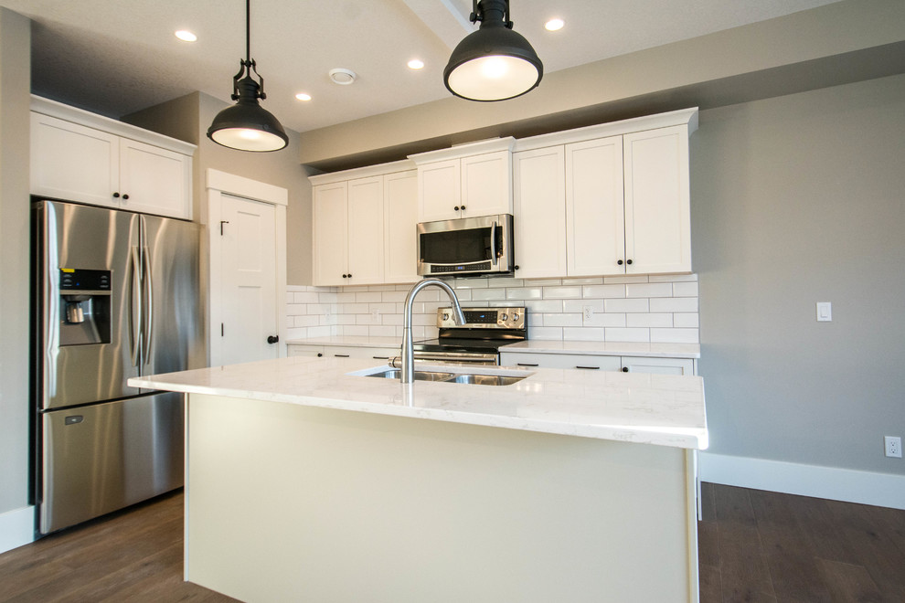 Mid-sized transitional single-wall medium tone wood floor and brown floor eat-in kitchen photo in Calgary with an undermount sink, shaker cabinets, gray cabinets, marble countertops, white backsplash, subway tile backsplash, stainless steel appliances, an island and white countertops