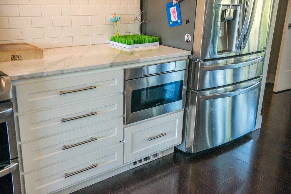 Open concept kitchen - huge transitional l-shaped dark wood floor and brown floor open concept kitchen idea in Chicago with a double-bowl sink, shaker cabinets, white cabinets, quartz countertops, white backsplash, ceramic backsplash, stainless steel appliances and an island