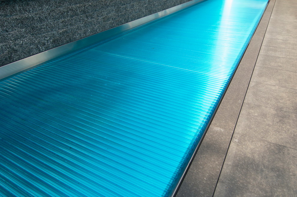 Modelo de piscina elevada contemporánea grande rectangular en patio con adoquines de piedra natural