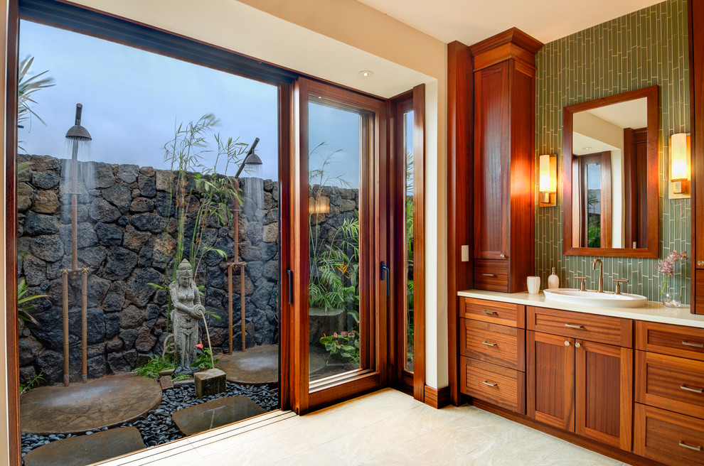 Photo of a large tropical master bathroom in Hawaii with shaker cabinets, dark wood cabinets, an alcove shower, a two-piece toilet, green tile, glass tile, white walls, porcelain floors, a vessel sink, engineered quartz benchtops, beige floor and a hinged shower door.