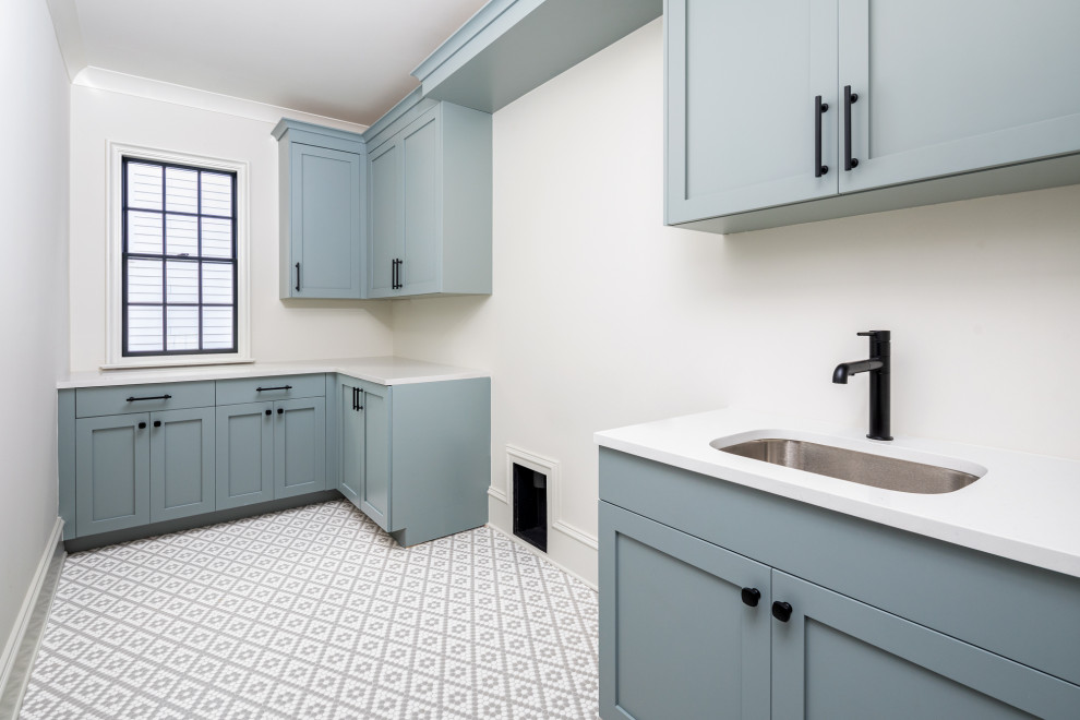Immagine di una sala lavanderia moderna di medie dimensioni con lavello da incasso, ante con riquadro incassato, ante blu, pareti bianche, pavimento con piastrelle in ceramica, lavatrice e asciugatrice affiancate, pavimento grigio e top bianco