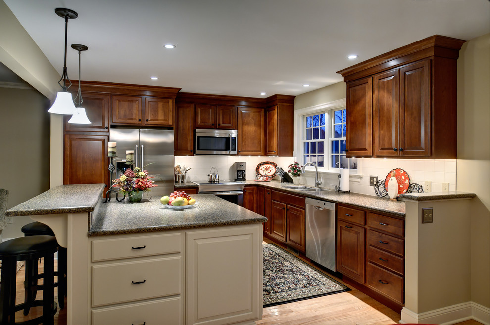 Inspiration for a mid-sized traditional u-shaped eat-in kitchen in Philadelphia with a double-bowl sink, raised-panel cabinets, dark wood cabinets, laminate benchtops, white splashback, porcelain splashback, stainless steel appliances, light hardwood floors and with island.
