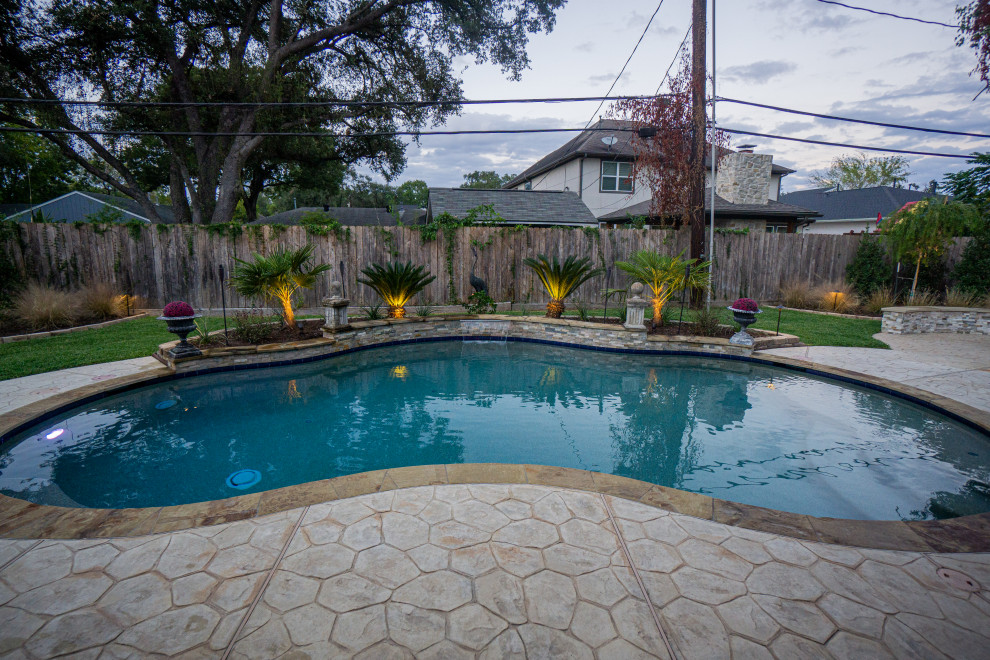 Ejemplo de piscinas y jacuzzis tropicales de tamaño medio tipo riñón en patio trasero con suelo de hormigón estampado