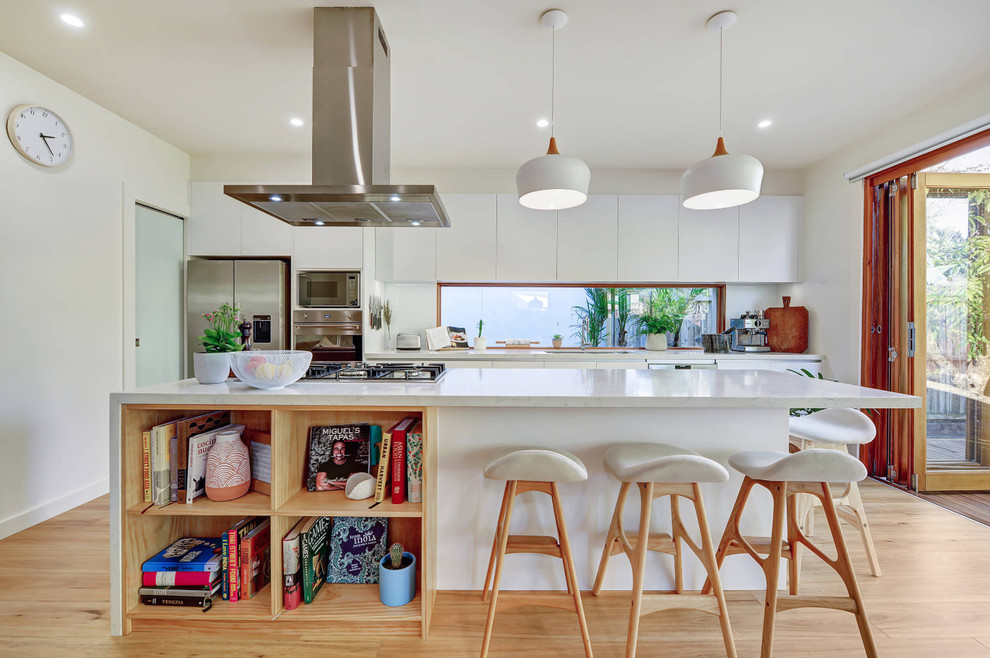 Design ideas for a contemporary galley kitchen in Sydney with an undermount sink, flat-panel cabinets, white cabinets, white splashback, window splashback, stainless steel appliances, medium hardwood floors, with island, brown floor and white benchtop.