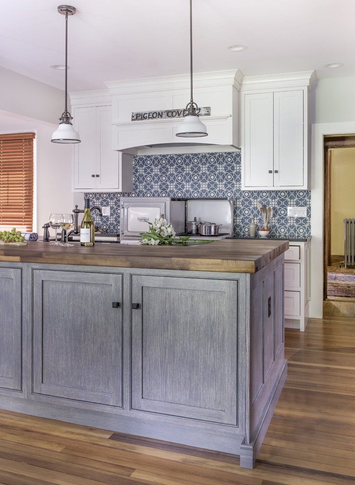 Design ideas for a mid-sized country galley open plan kitchen in Boston with a farmhouse sink, beaded inset cabinets, white cabinets, wood benchtops, blue splashback, cement tile splashback, panelled appliances, medium hardwood floors, with island, brown floor and black benchtop.