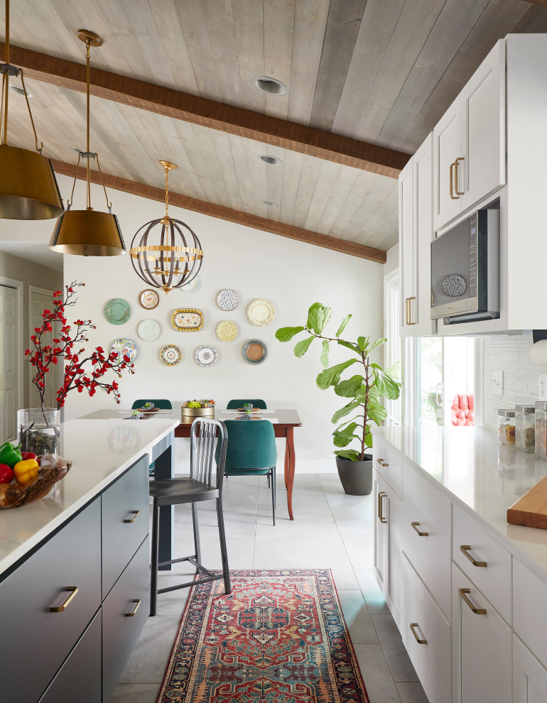 Inspiration for a mid-sized transitional u-shaped ceramic tile, gray floor and vaulted ceiling eat-in kitchen remodel with an undermount sink, shaker cabinets, white cabinets, quartz countertops, white backsplash, glass tile backsplash, stainless steel appliances, an island and white countertops