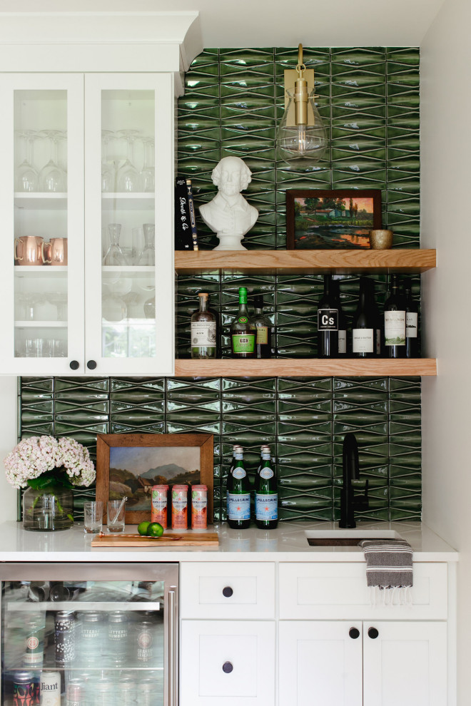 This is an example of a mid-sized transitional single-wall wet bar in Denver with an undermount sink, glass-front cabinets, white cabinets, green splashback, porcelain splashback and white benchtop.