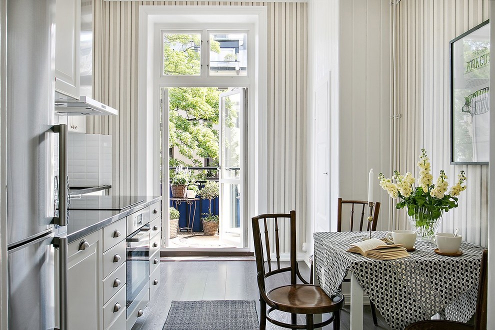 Inspiration for a traditional single-wall eat-in kitchen in Stockholm with raised-panel cabinets, white cabinets, stainless steel benchtops, white splashback, stainless steel appliances, dark hardwood floors, black floor and grey benchtop.