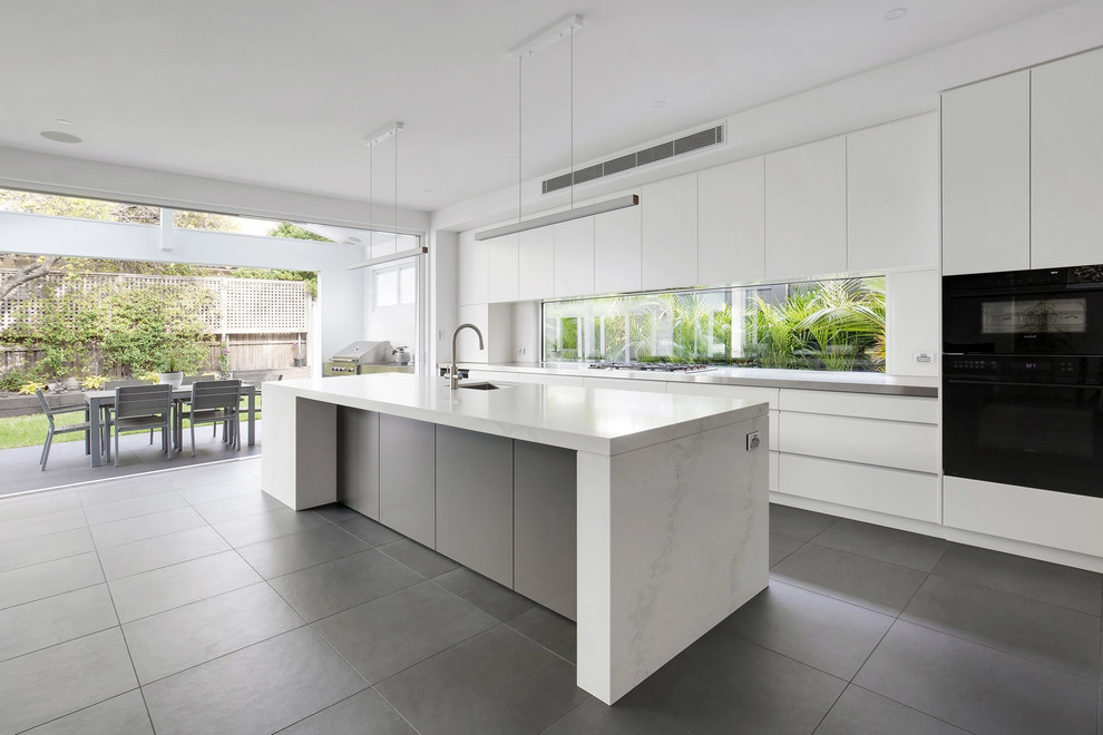 Photo of a large modern l-shaped open plan kitchen in Sydney with an undermount sink, flat-panel cabinets, grey cabinets, quartz benchtops, white splashback, window splashback, black appliances, porcelain floors, with island, grey floor and white benchtop.