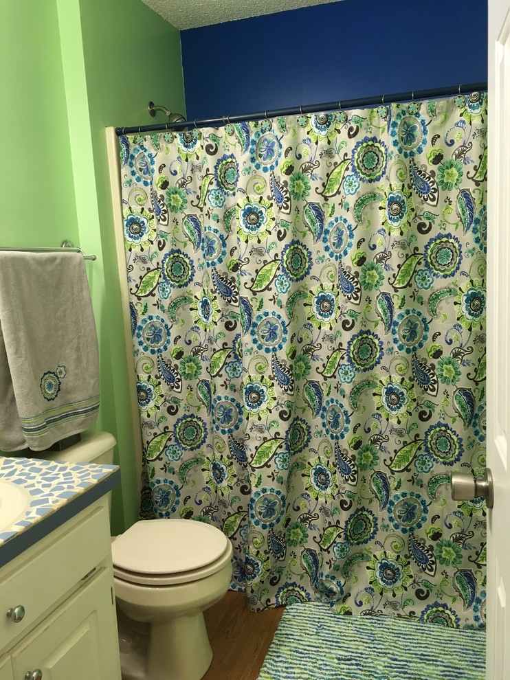 Transitional laminate floor and brown floor tub/shower combo photo with recessed-panel cabinets, white cabinets, blue walls, a drop-in sink, tile countertops and blue countertops