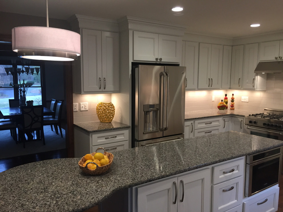 Transitional dark wood floor kitchen photo with an undermount sink, flat-panel cabinets, white cabinets, granite countertops, white backsplash, porcelain backsplash, stainless steel appliances and an island